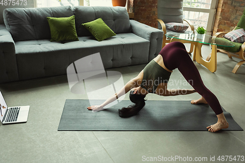 Image of Sporty young woman taking yoga lessons online and practice at home