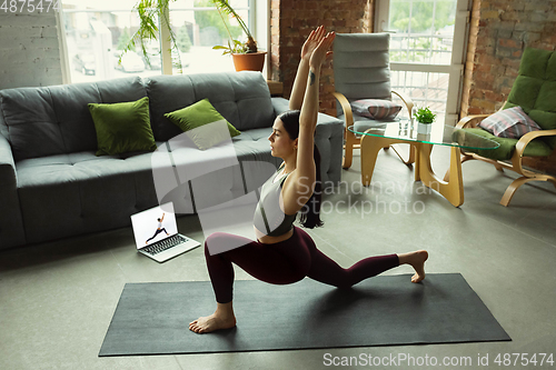 Image of Sporty young woman taking yoga lessons online and practice at home