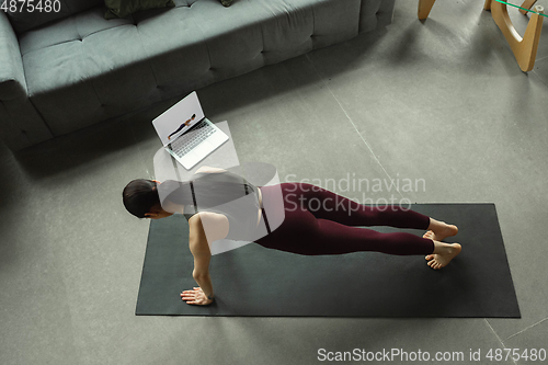 Image of Sporty young woman taking yoga lessons online and practice at home