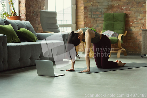 Image of Sporty young woman taking yoga lessons online and practice at home