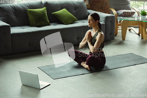 Image of Sporty young woman taking yoga lessons online and practice at home