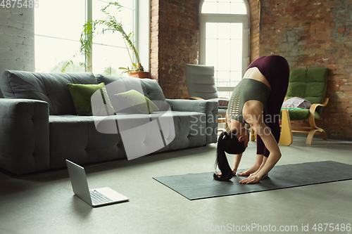 Image of Sporty young woman taking yoga lessons online and practice at home