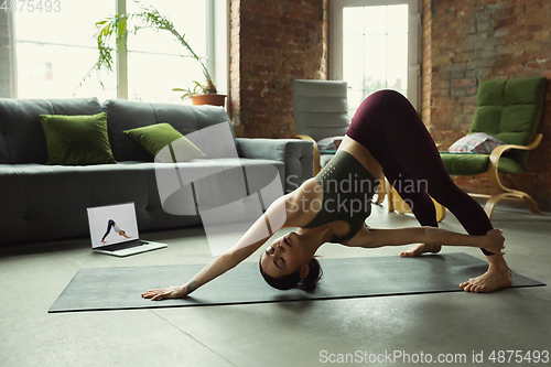 Image of Sporty young woman taking yoga lessons online and practice at home