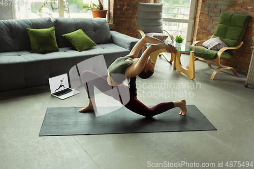 Image of Sporty young woman taking yoga lessons online and practice at home