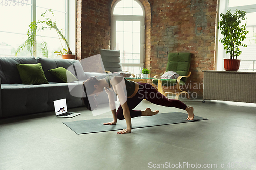 Image of Sporty young woman taking yoga lessons online and practice at home