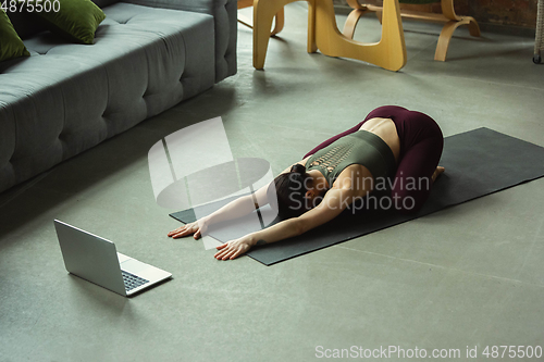 Image of Sporty young woman taking yoga lessons online and practice at home