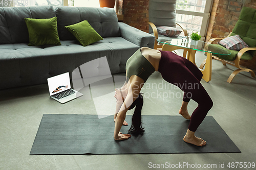 Image of Sporty young woman taking yoga lessons online and practice at home