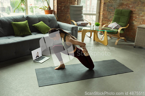 Image of Sporty young woman taking yoga lessons online and practice at home