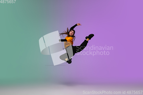 Image of Girl dancing hip-hop in stylish clothes on gradient background at dance hall in neon light.