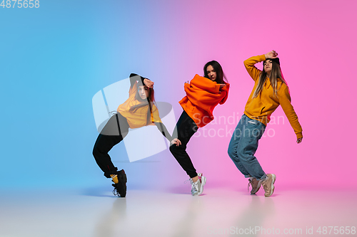 Image of Girls dancing hip-hop in stylish clothes on gradient background at dance hall in neon light.