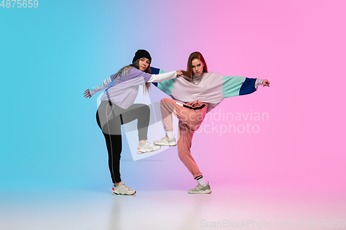 Image of Girls dancing hip-hop in stylish clothes on gradient background at dance hall in neon light.