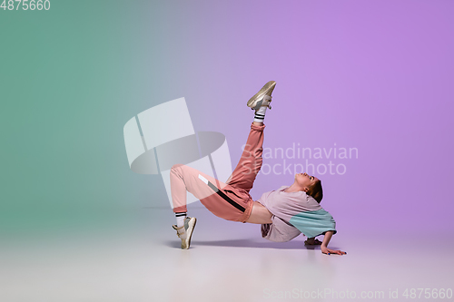 Image of Girl dancing hip-hop in stylish clothes on gradient background at dance hall in neon light.