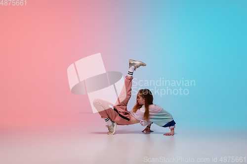 Image of Girl dancing hip-hop in stylish clothes on gradient background at dance hall in neon light.