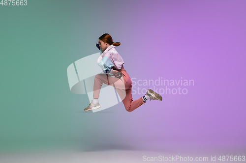 Image of Girl dancing hip-hop in stylish clothes on gradient background at dance hall in neon light.