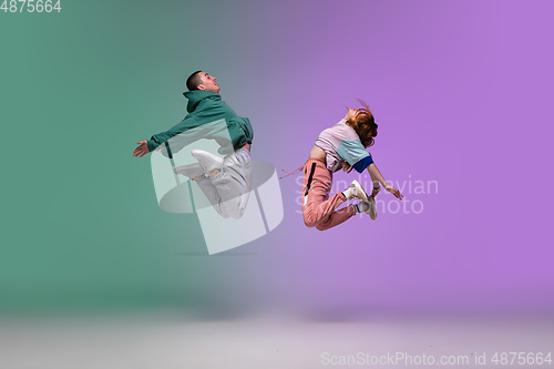 Image of Boy and girl dancing hip-hop in stylish clothes on gradient background at dance hall in neon light.