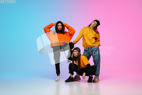 Image of Girls dancing hip-hop in stylish clothes on gradient background at dance hall in neon light.