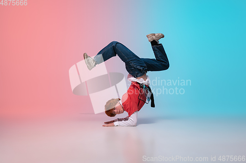 Image of Boy dancing hip-hop in stylish clothes on gradient background at dance hall in neon light.