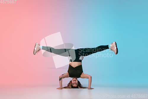 Image of Girl dancing hip-hop in stylish clothes on gradient background at dance hall in neon light.