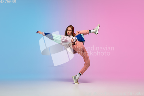 Image of Girl dancing hip-hop in stylish clothes on gradient background at dance hall in neon light.