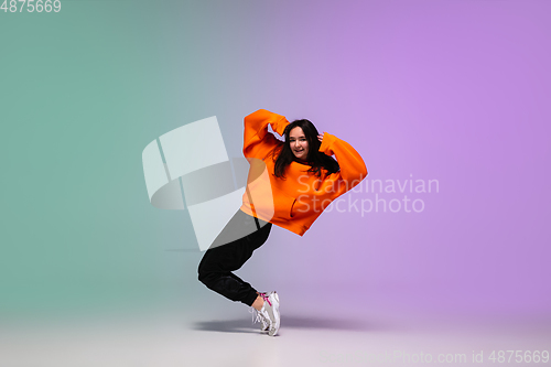 Image of Girl dancing hip-hop in stylish clothes on gradient background at dance hall in neon light.