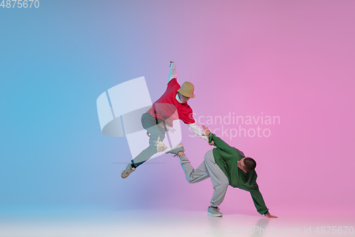 Image of Boys dancing hip-hop in stylish clothes on gradient background at dance hall in neon light.
