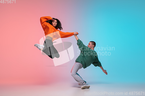 Image of Boy and girl dancing hip-hop in stylish clothes on gradient background at dance hall in neon light.