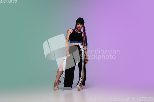 Image of Girl dancing hip-hop in stylish clothes on gradient background at dance hall in neon light.