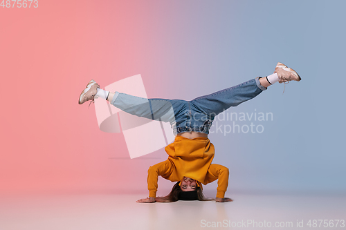 Image of Girl dancing hip-hop in stylish clothes on gradient background at dance hall in neon light.