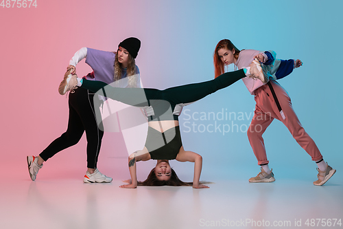 Image of Girls dancing hip-hop in stylish clothes on gradient background at dance hall in neon light.