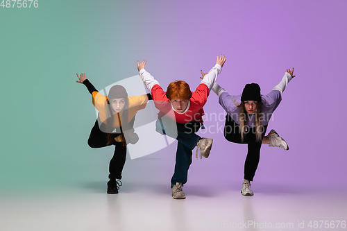 Image of Group of teens, boys and girls dancing hip-hop in stylish clothes on gradient studio background in neon light.