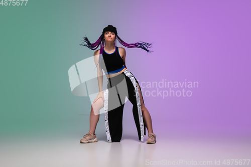 Image of Girl dancing hip-hop in stylish clothes on gradient background at dance hall in neon light.