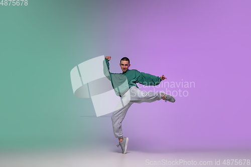 Image of Boy dancing hip-hop in stylish clothes on gradient background at dance hall in neon light.