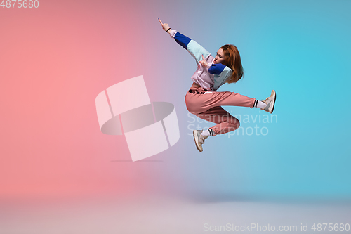 Image of Girl dancing hip-hop in stylish clothes on gradient background at dance hall in neon light.