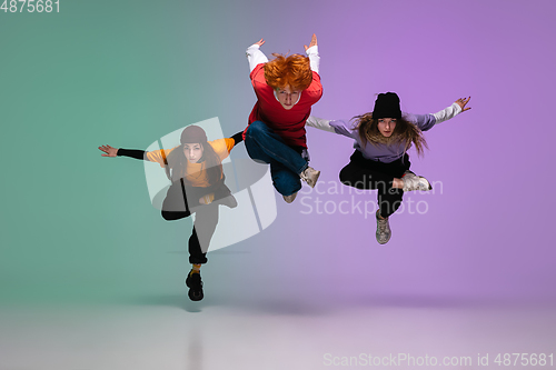 Image of Group of teens, boys and girls dancing hip-hop in stylish clothes on gradient studio background in neon light.