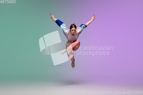Image of Girl dancing hip-hop in stylish clothes on gradient background at dance hall in neon light.