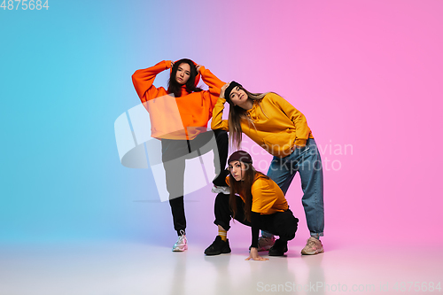 Image of Girls dancing hip-hop in stylish clothes on gradient background at dance hall in neon light.