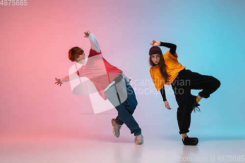 Image of Boy and girl dancing hip-hop in stylish clothes on gradient background at dance hall in neon light.