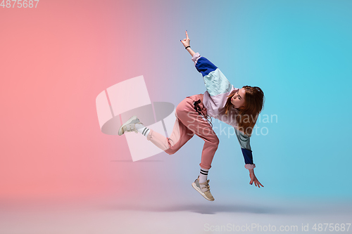 Image of Girl dancing hip-hop in stylish clothes on gradient background at dance hall in neon light.