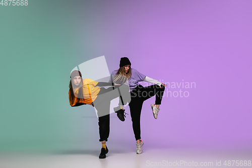 Image of Girls dancing hip-hop in stylish clothes on gradient background at dance hall in neon light.