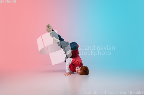 Image of Boy dancing hip-hop in stylish clothes on gradient background at dance hall in neon light.