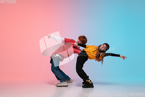 Image of Boy and girl dancing hip-hop in stylish clothes on gradient background at dance hall in neon light.