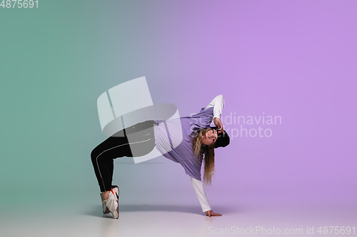 Image of Girl dancing hip-hop in stylish clothes on gradient background at dance hall in neon light.