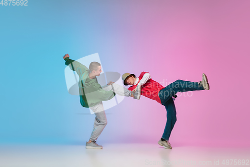 Image of Boys dancing hip-hop in stylish clothes on gradient background at dance hall in neon light.