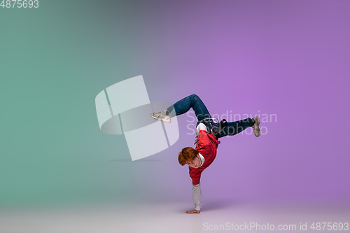 Image of Boy dancing hip-hop in stylish clothes on gradient background at dance hall in neon light.