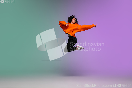 Image of Girl dancing hip-hop in stylish clothes on gradient background at dance hall in neon light.