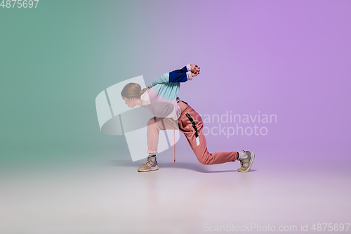 Image of Girl dancing hip-hop in stylish clothes on gradient background at dance hall in neon light.