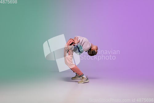 Image of Girl dancing hip-hop in stylish clothes on gradient background at dance hall in neon light.