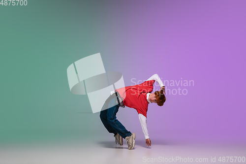 Image of Boy dancing hip-hop in stylish clothes on gradient background at dance hall in neon light.