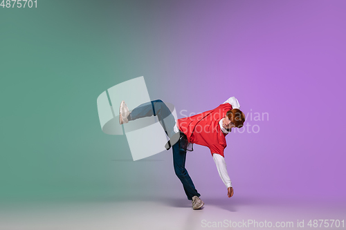 Image of Boy dancing hip-hop in stylish clothes on gradient background at dance hall in neon light.