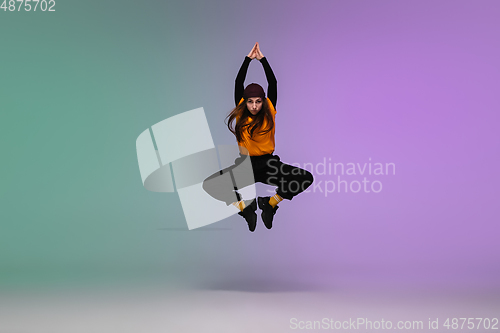 Image of Girl dancing hip-hop in stylish clothes on gradient background at dance hall in neon light.